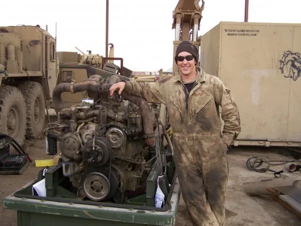Bill Swift in coveralls beside a pulled HEMTT diesel engine.